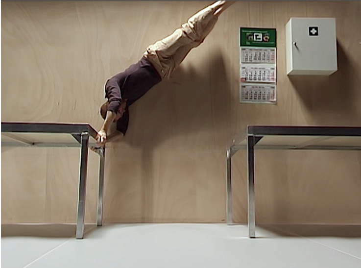 You can see a person between two tables. She is leaning on one of the tables, stretching her body upwards. 