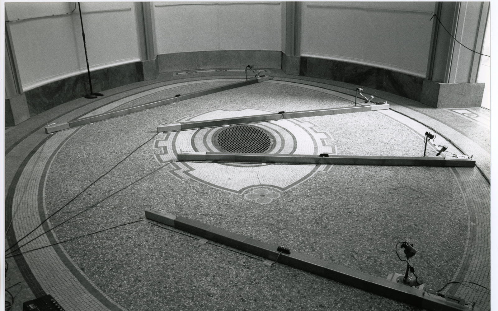 Man sieht das Werk »Number Made Audible«. Das schwarz-weiß Foto zeigt einen runden Raum. Auf dem Boden befinden sich vier lange Stelzen, an denen Kabel befestigt sind.