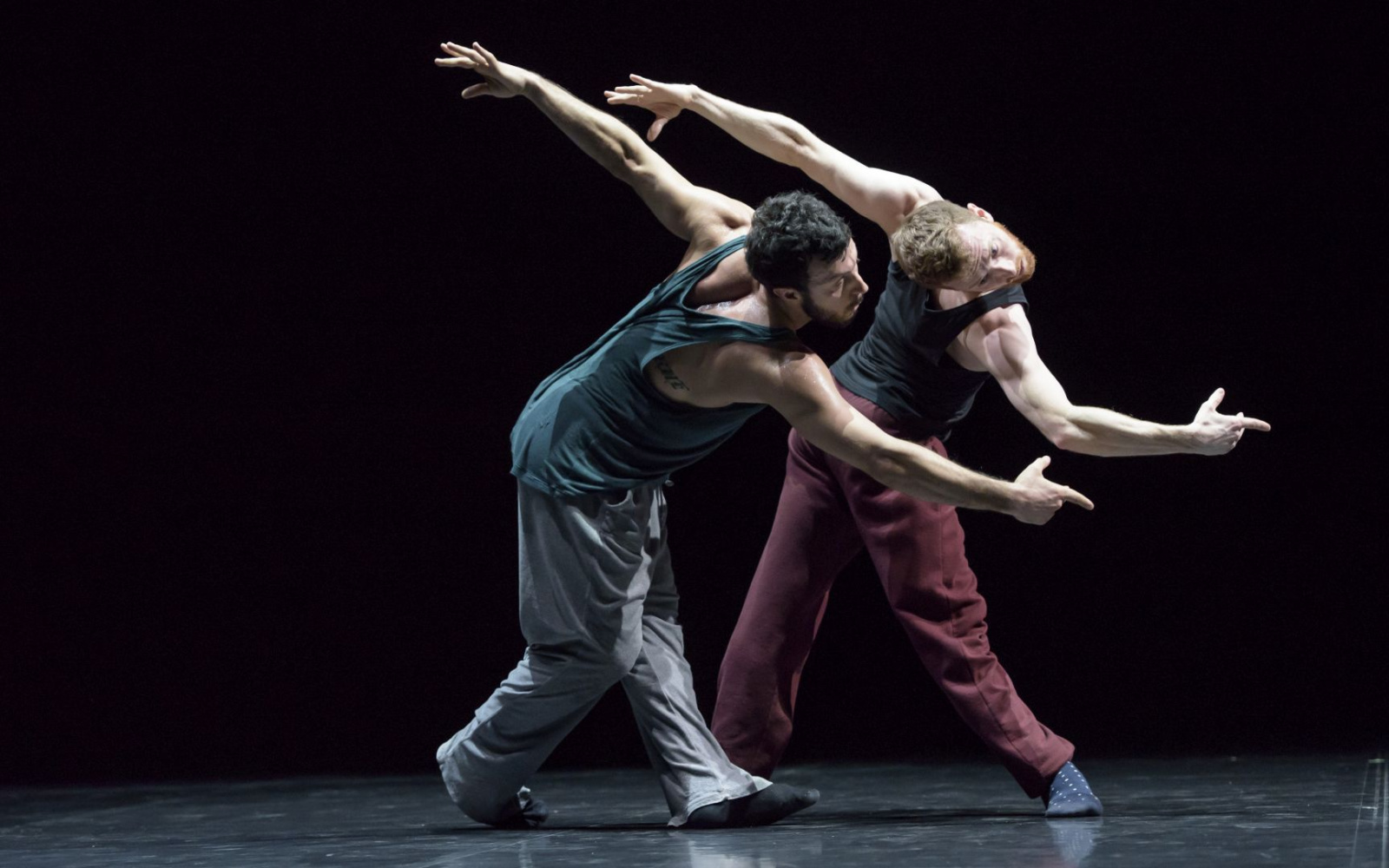 Two dancers in the choreography »Friends of Forsythe«. They stand together on a black stage and artfully contort their bodies parallel to each other.