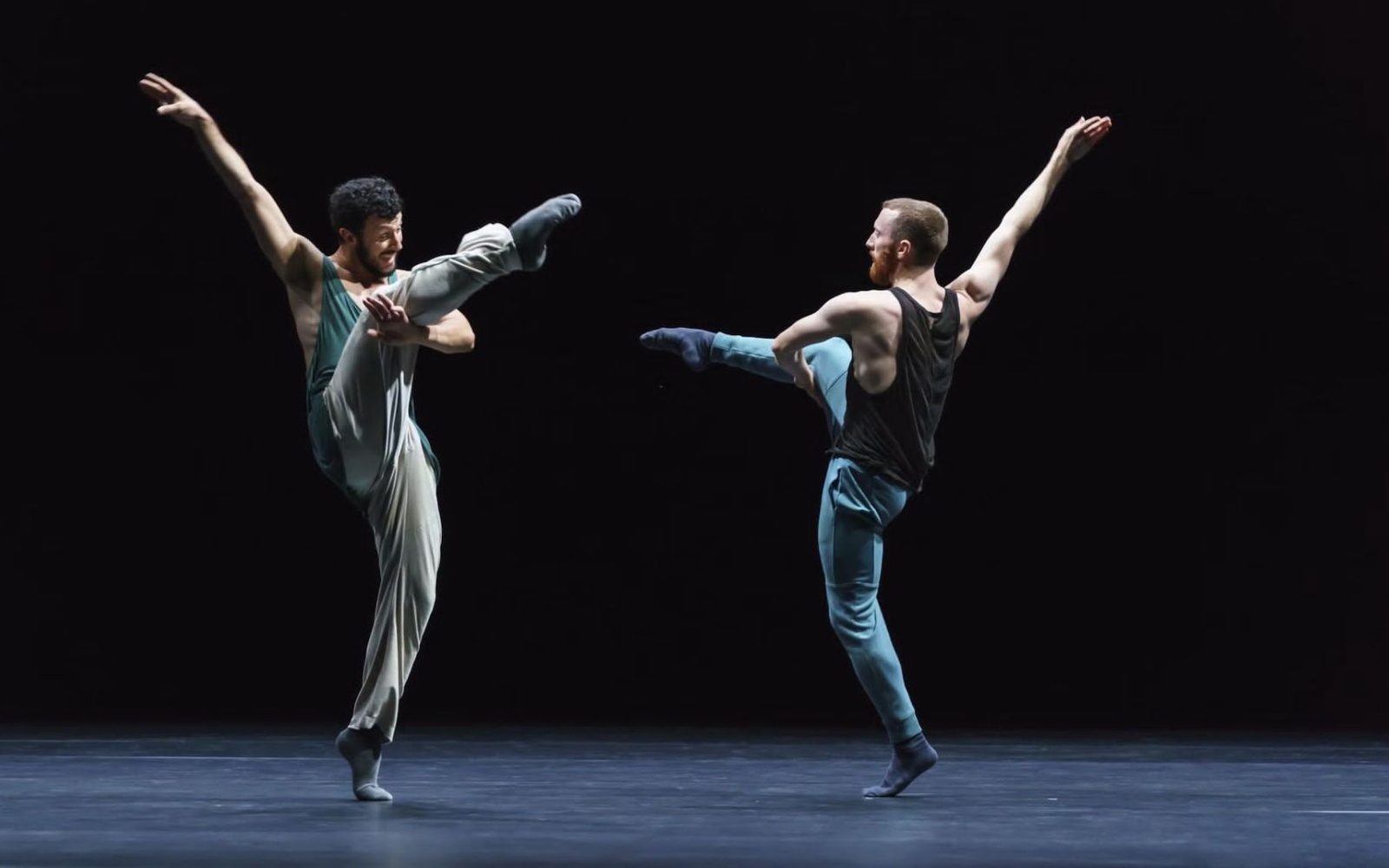 Zwei Tänzer der Choreografie »Friends of Forsythe«. Sie stehen sich gegenüber auf einer schwarzen Bühne und heben kunstvoll ihre Arme und Beine in die Höhe.