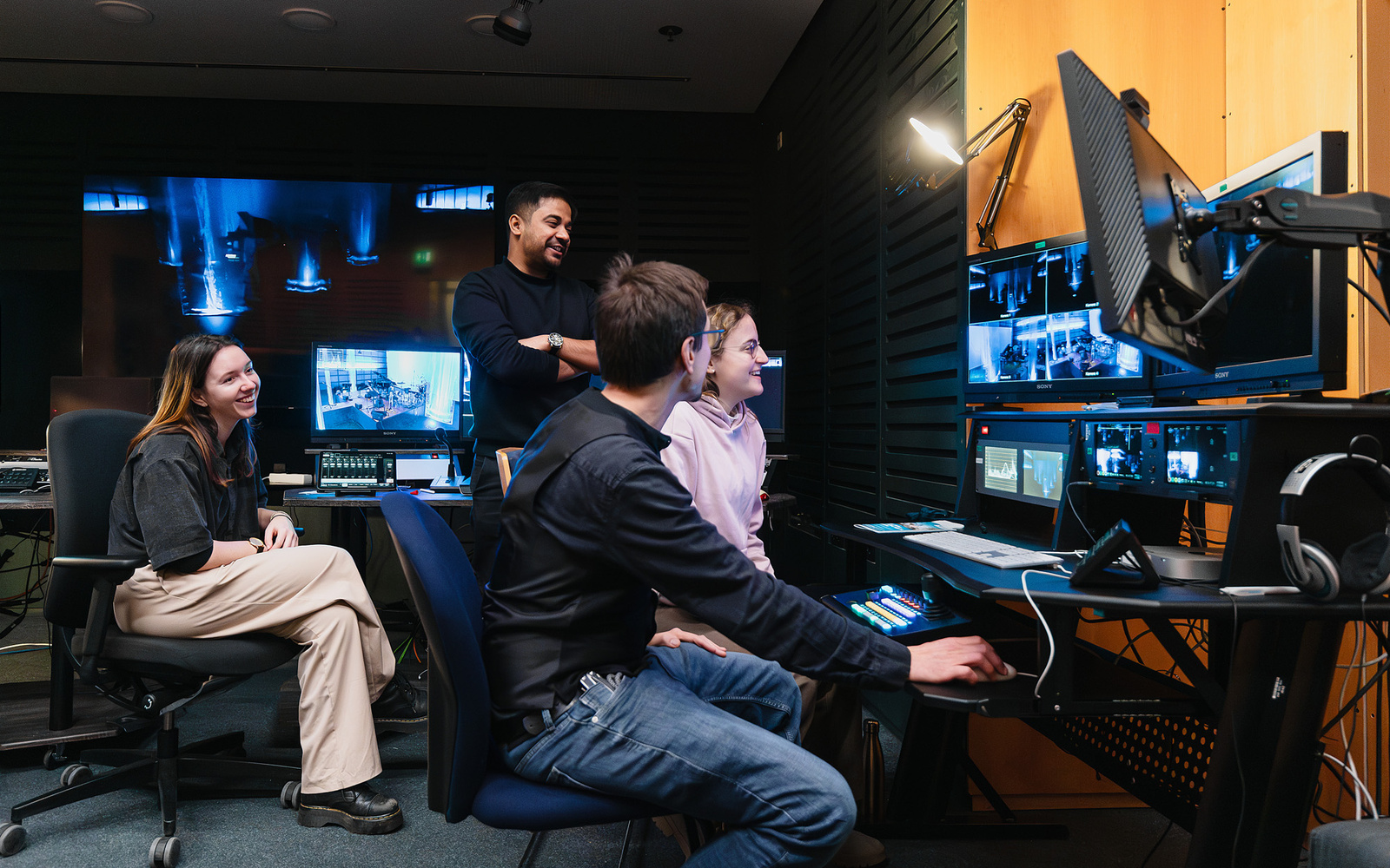 Das Bild zeigt die Mitarbeiter:innen des Videostudios im Regieraum auf Monitore blickend.