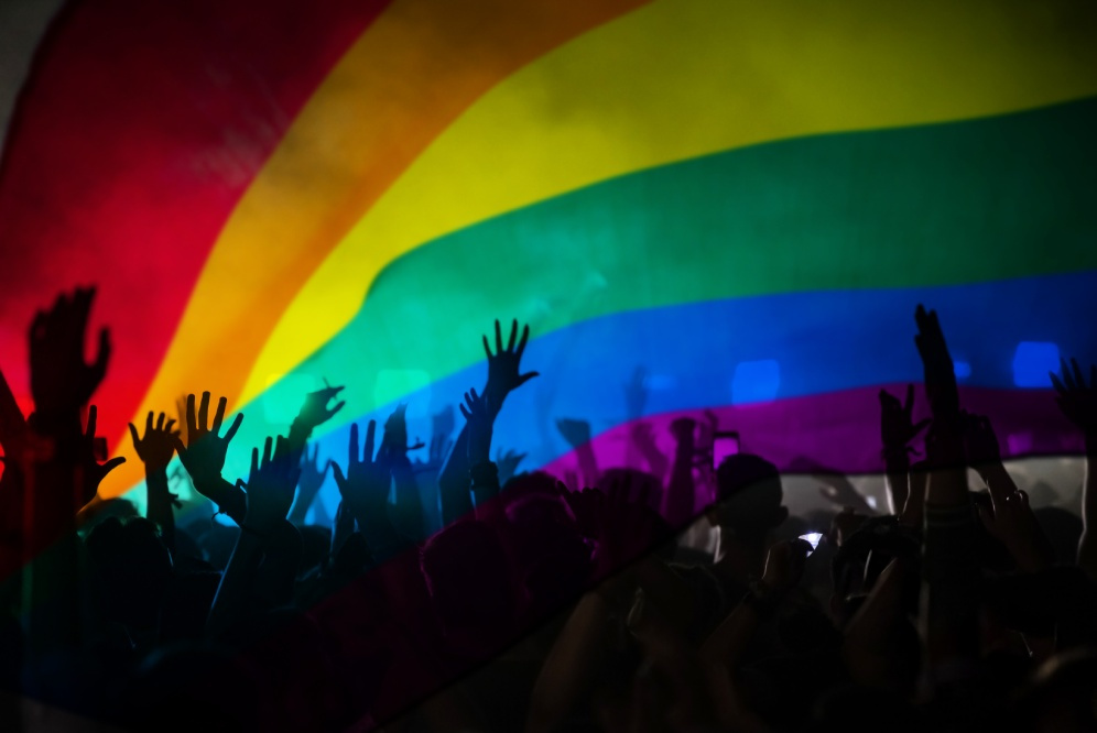 Hands can be seen in front of a rainbow flag.