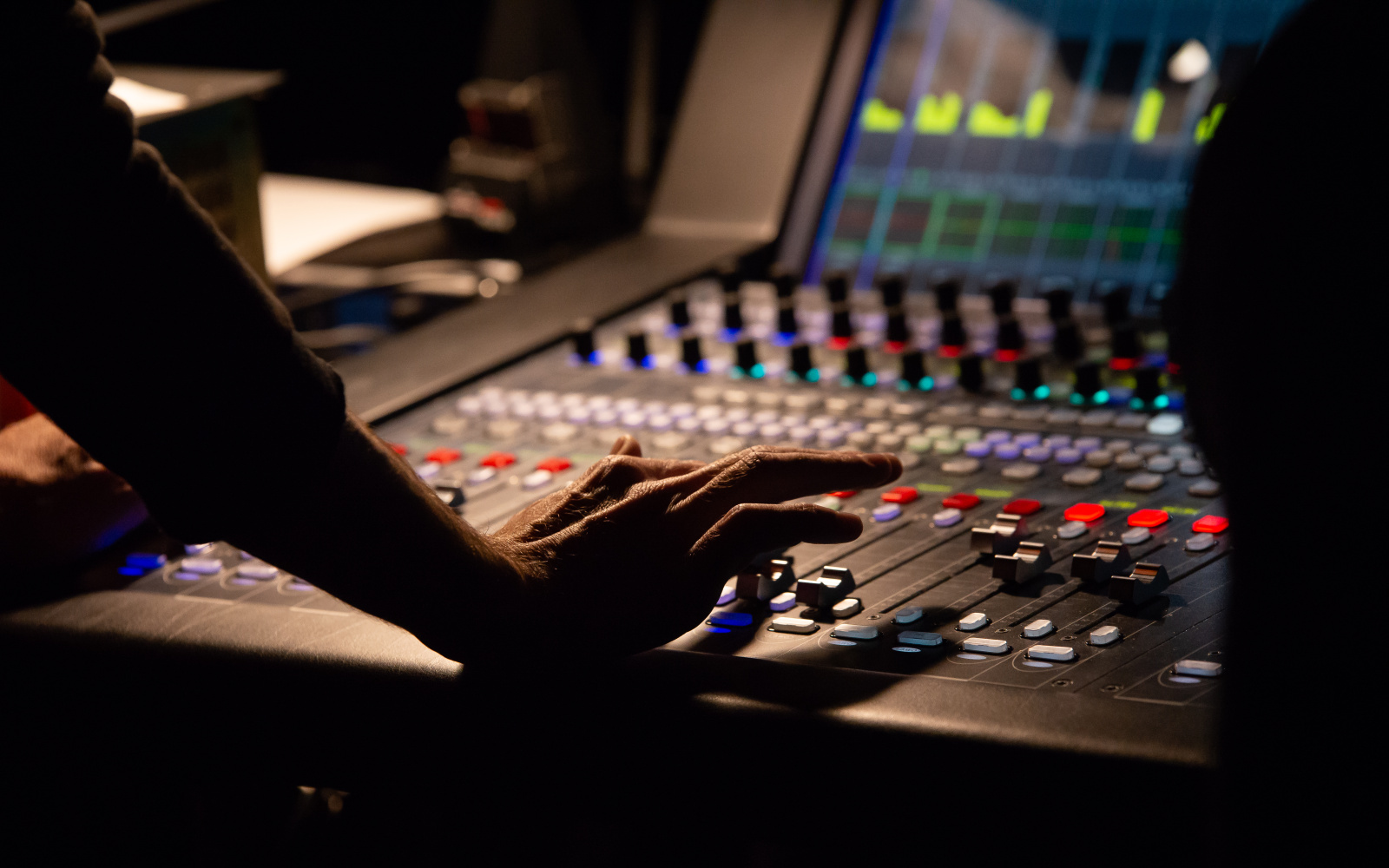 A hand operates a sound mixer in the dark at an event