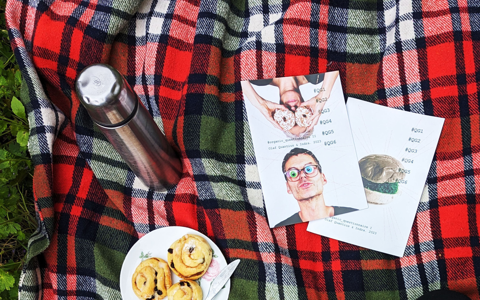 A red and green checkered picnic blanket from above with flyers, thermos flask and coffee.