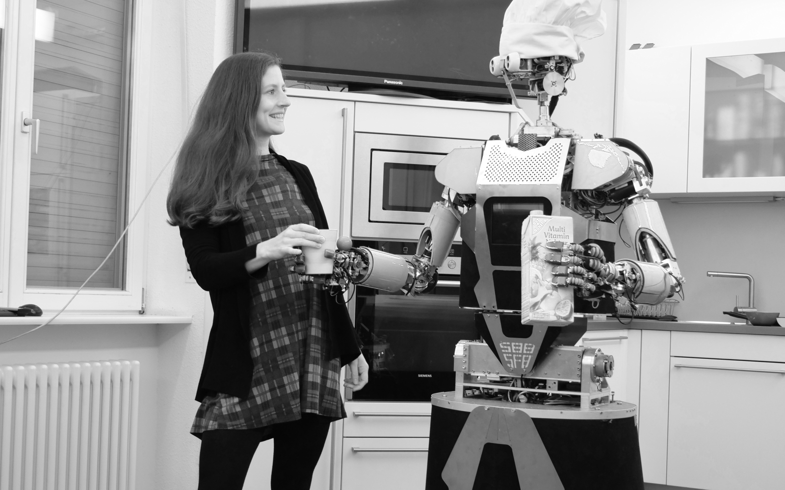 Schwarz-weiß Fotografie von Franziska Krebs und einem humanoiden Roboter, der ihr einen Becher Saft reicht. 