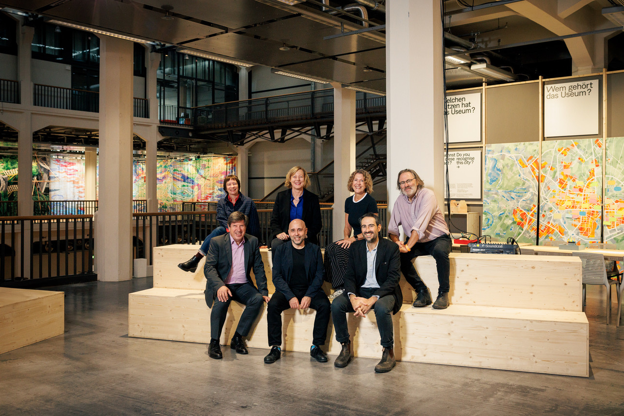 Seven people are seen sitting in two rows on a wooden bench.