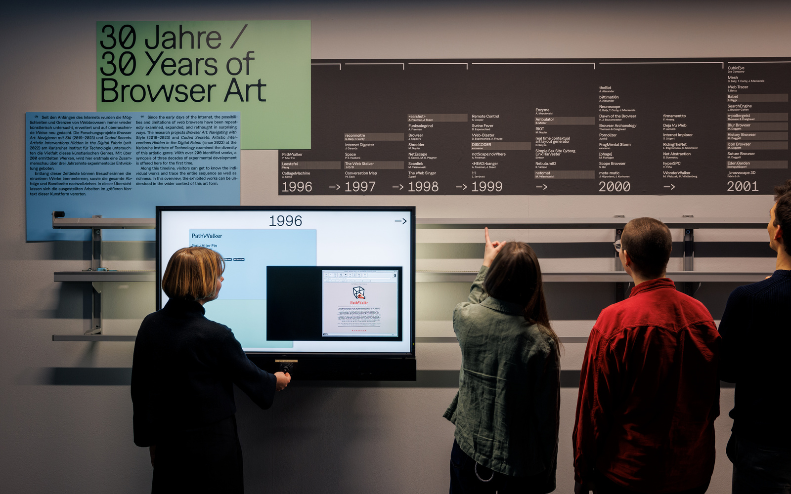Ein Zeitstrahl an der Wand davor ein Bildschirm und Personen von hinten.