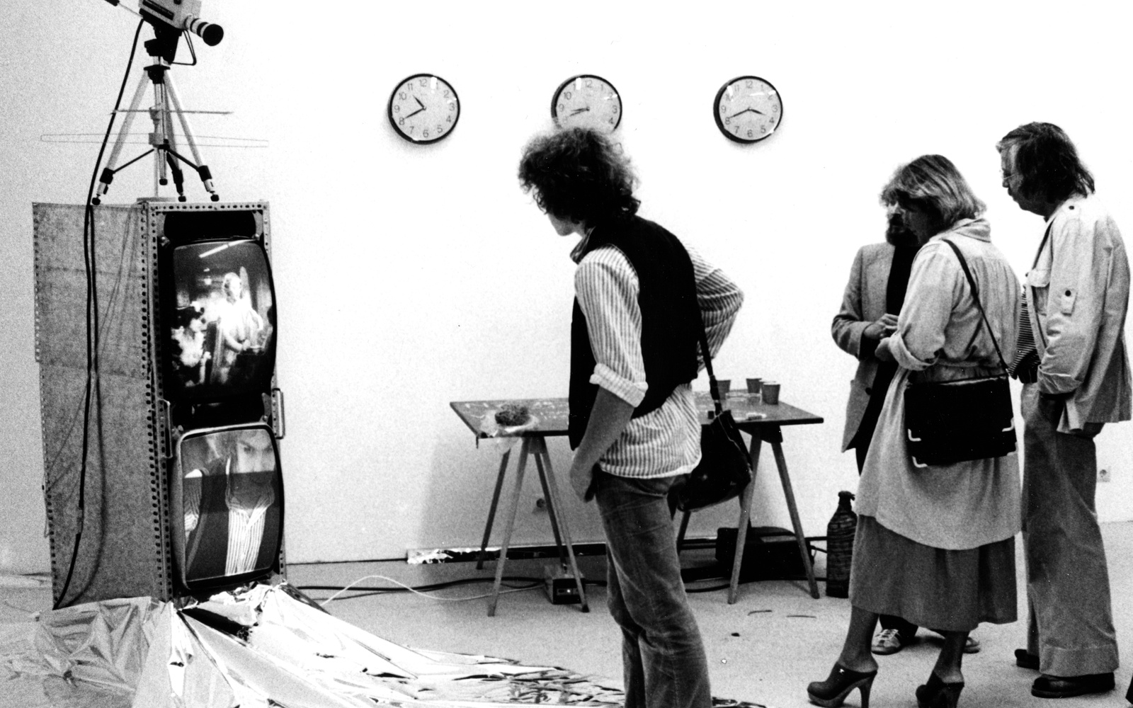 Schwarz-Weiß-Aufnahme von vier Personen, die auf eine Videoinstallation blicken. 