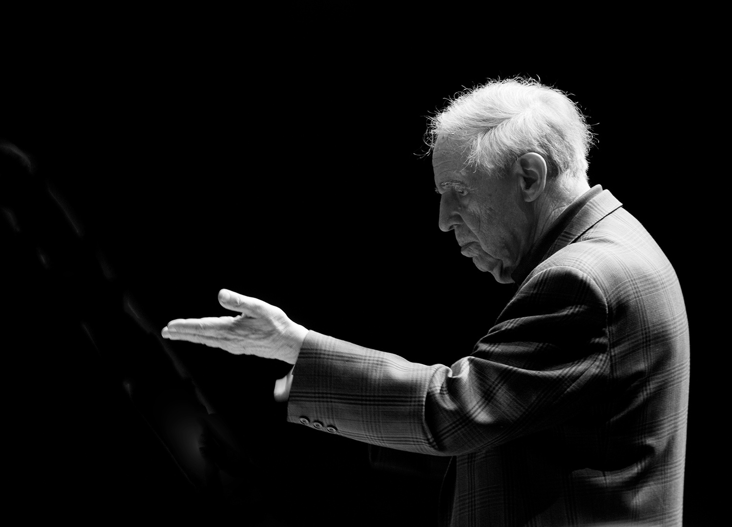 Pierre Boulez in Seitenansicht: Er hebt eine Hand, die Handfläche nach oben.