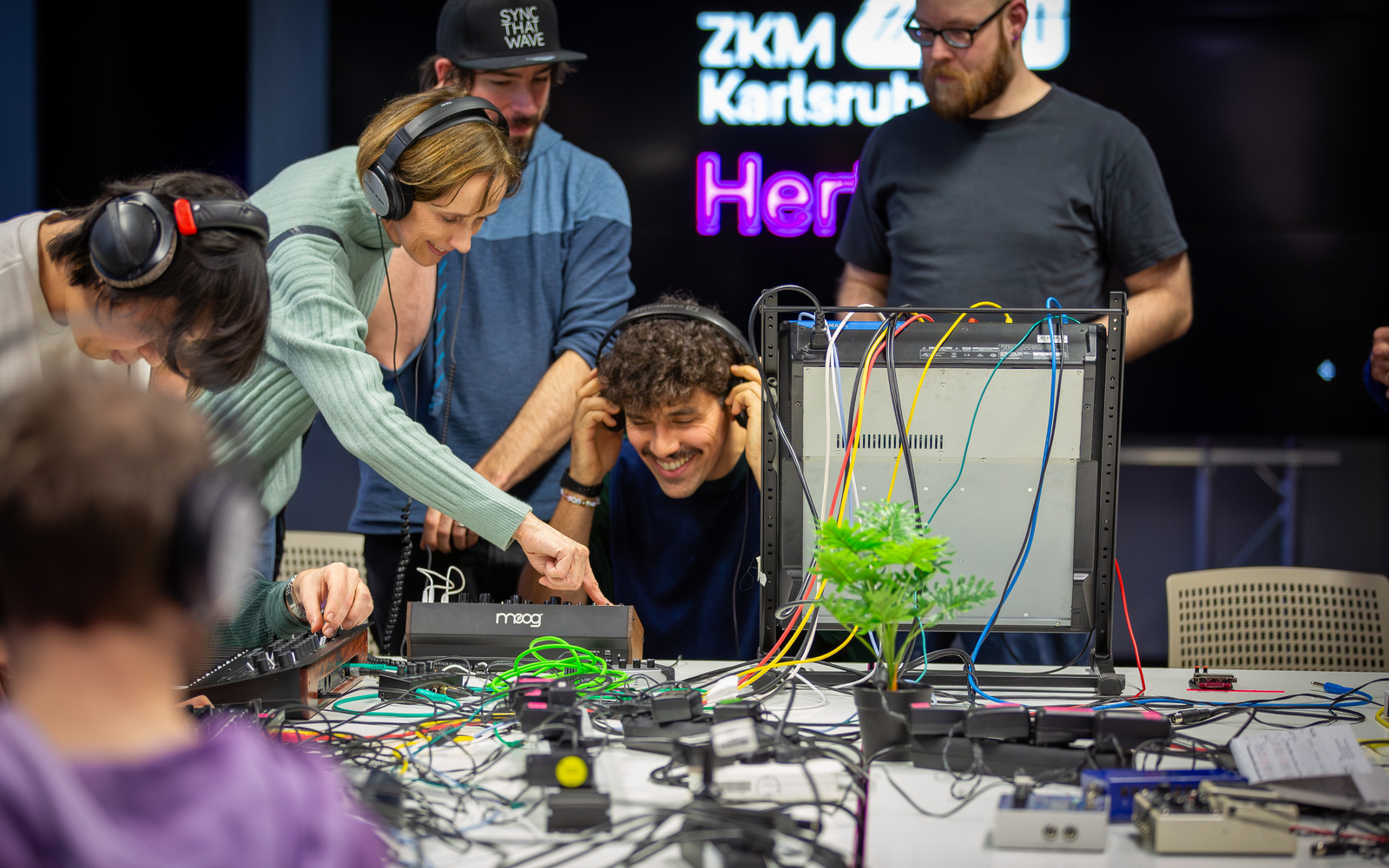 The picture shows a group of people during a jam session, surrounded by colorful cables in a lively atmosphere.
