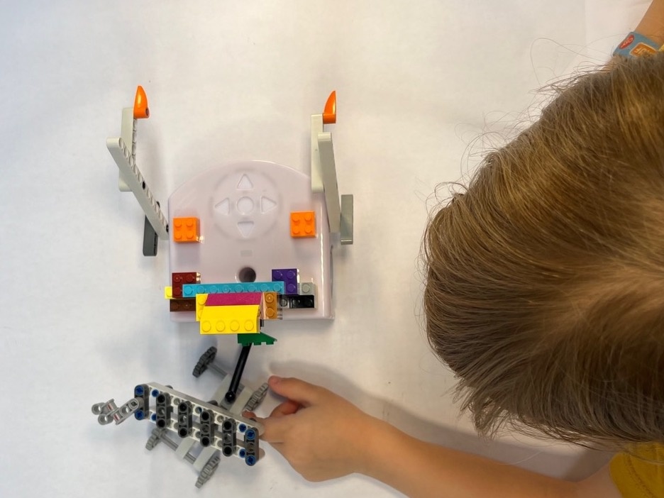 Ein Kind ist zu sehen, welches auf einem Blatt Papier zusammen mit dem Thymio-Roboter malt.