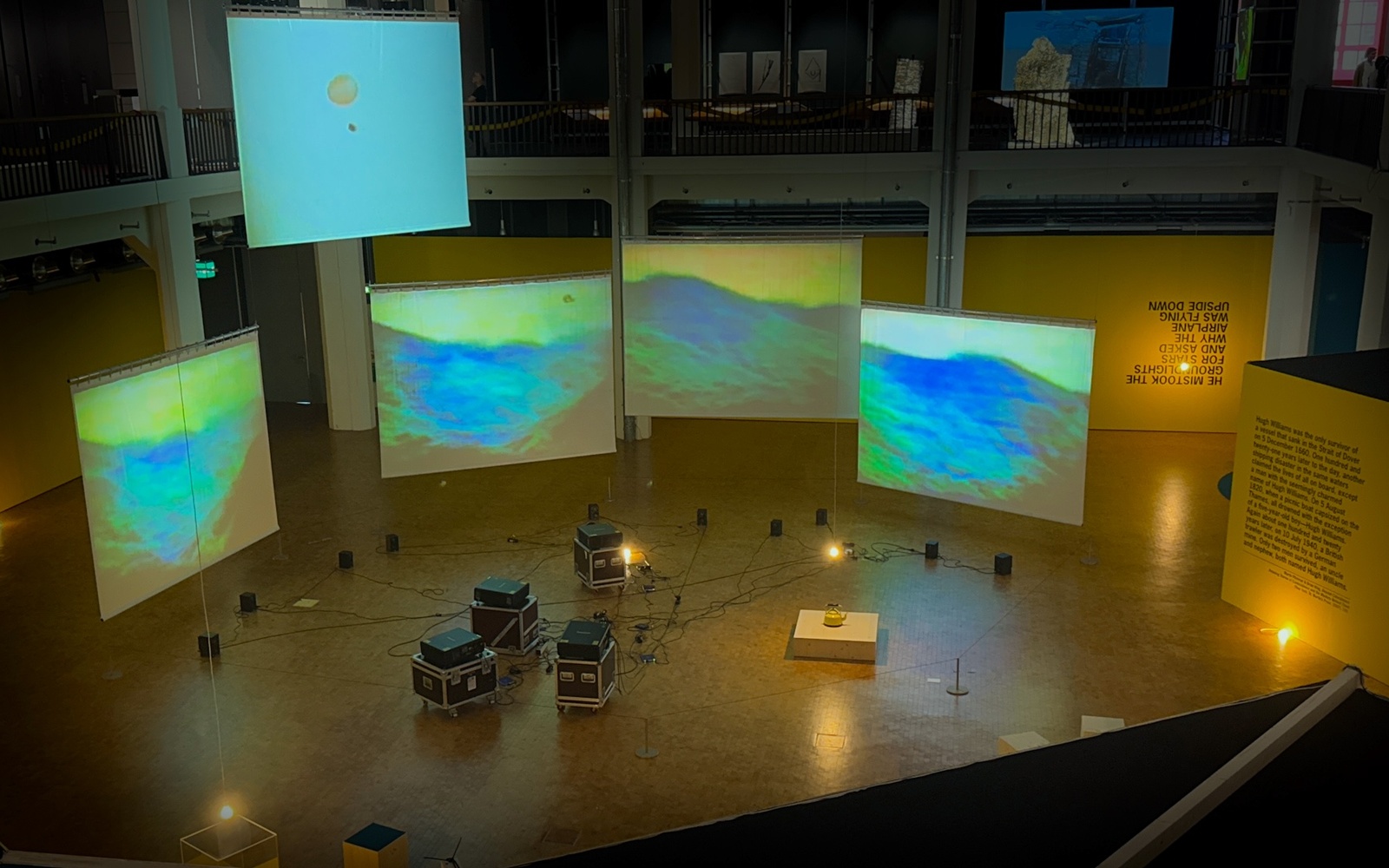 Ausstellungsansicht mit gelben Wänden und beleuchteten Leinwänden.