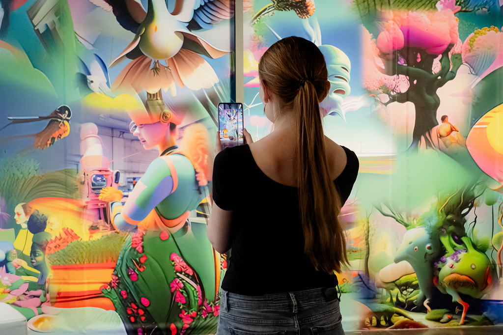 Eine Person mit Smartphone fotografiert eine bunte Bildwand.