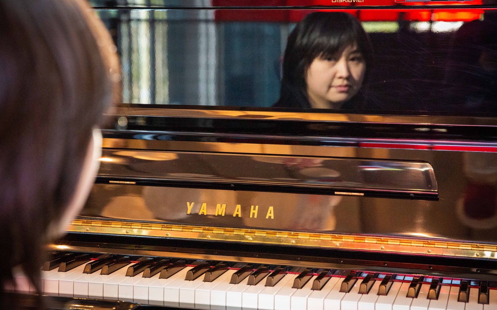 A piano can be seen, reflecting the face of a person.