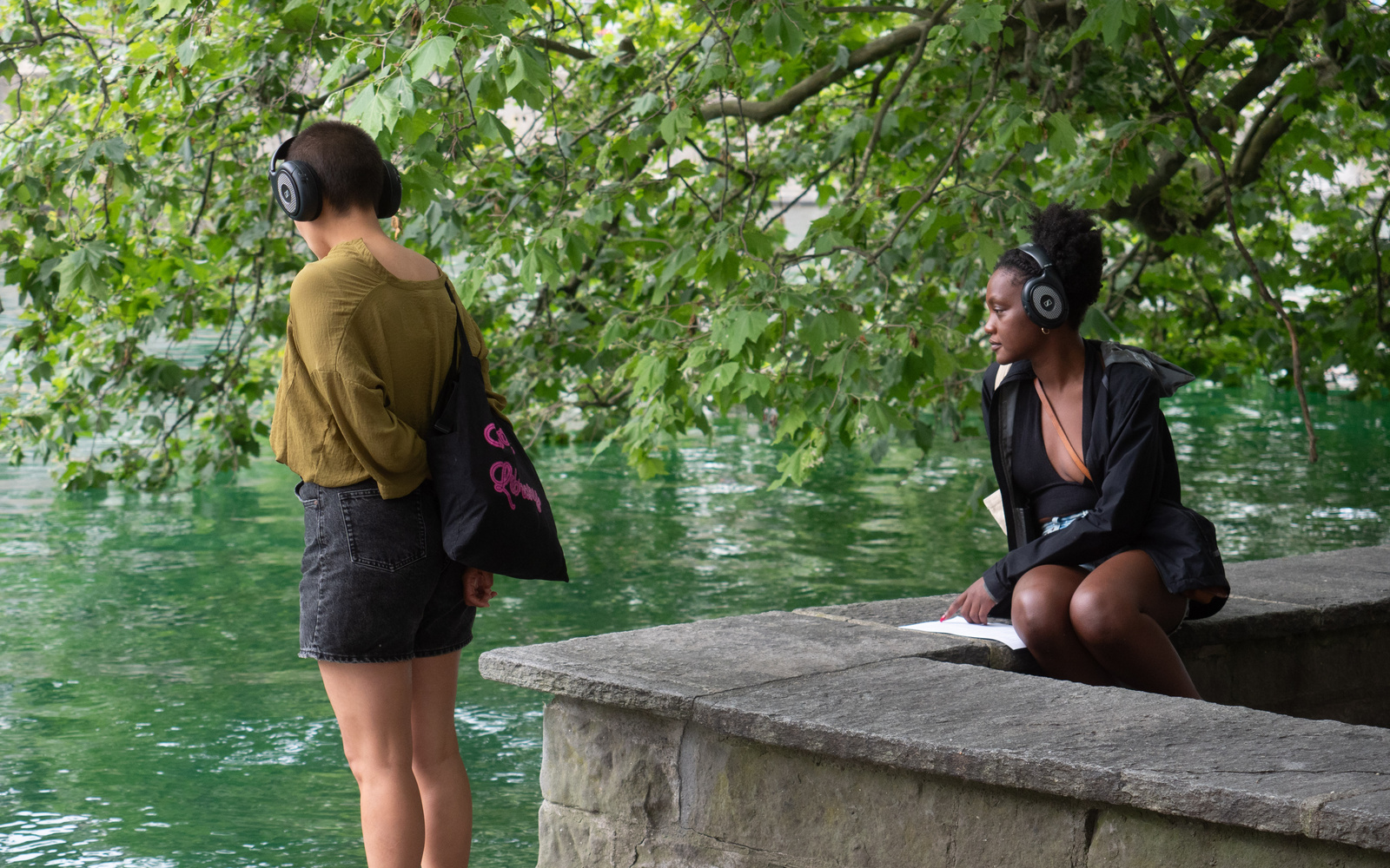 You can see two people wearing headphones and looking at a river.