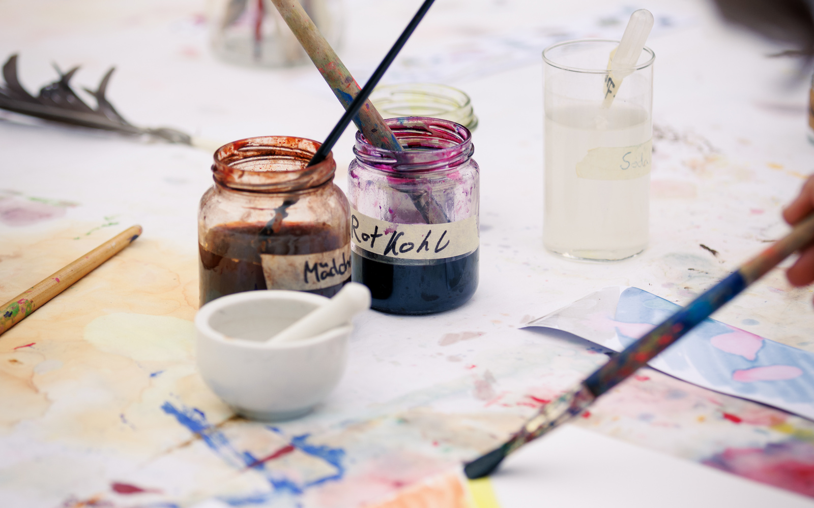 The picture shows paintbrushes and jars filled with paint on a table.  