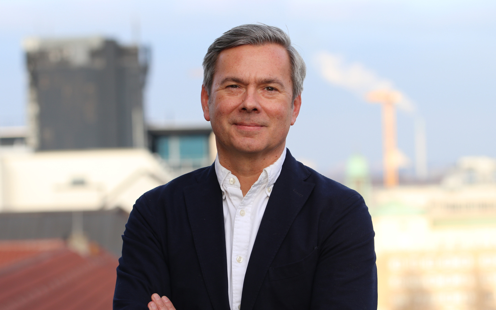 Holger Neinhaus steht mit verschränkten Armen vor einer Skyline.
