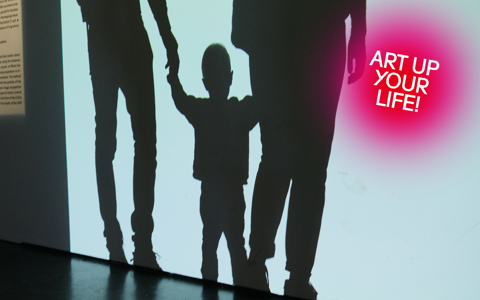 Schatten eines Kindes, das die Hände zweier Erwachsenen hält vor weißem Hintergrund.