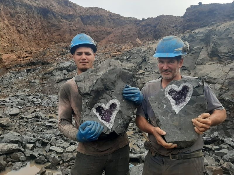 Two people wearing helmets can be seen holding pieces of rock up to the camera.