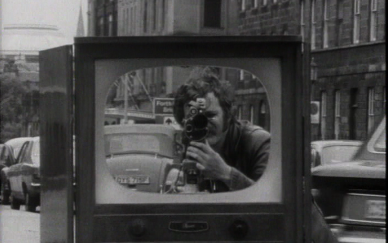 Zu sehen ist eine Schwarz-Weiß-Aufnahme, die einen Fernseher auf einer Straße zeigt.