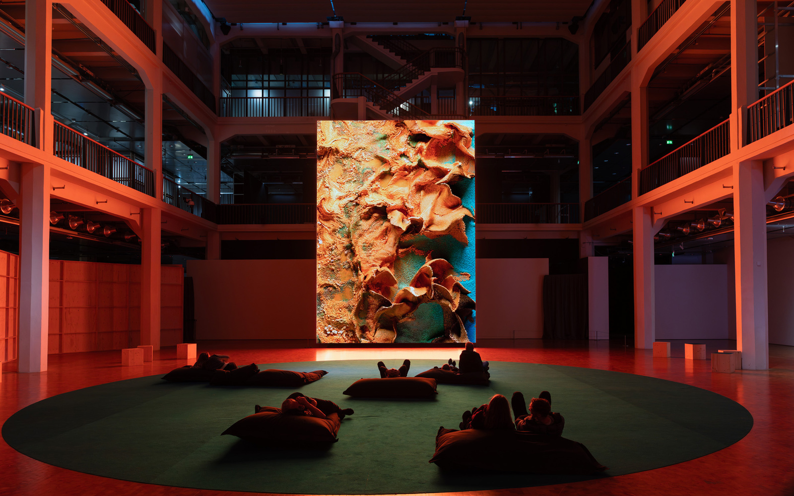 Personen sitzen vor einem riesigen Bildschirm, auf dem ein abstraktes Kunstwerk zu sehen ist.