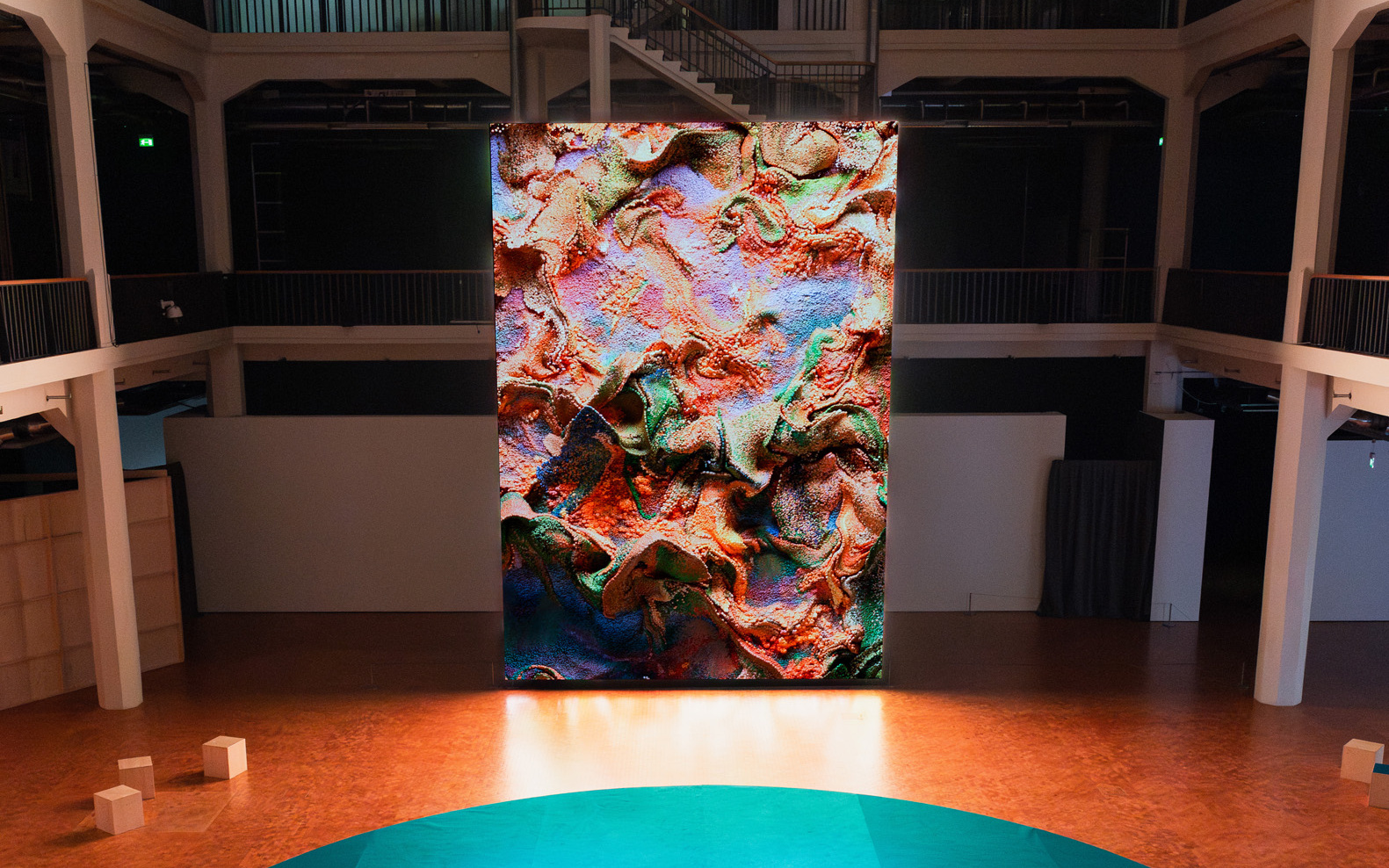 Einige Personen sitzen vor einem riesigen Bildschirm, auf dem ein abstraktes Kunstwerk zu sehen ist.