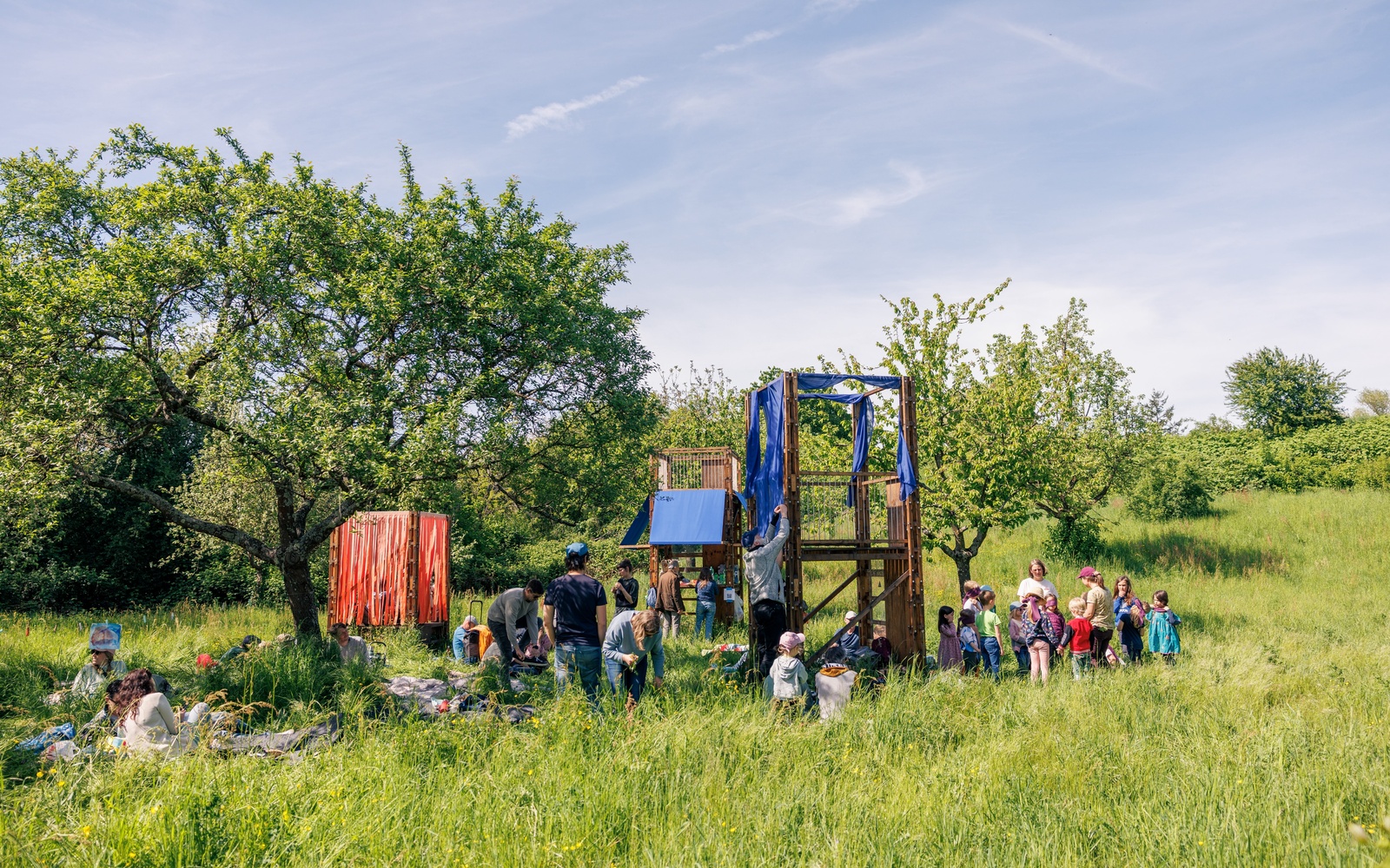 Kinder und Erwachsene auf einer Wiese mit Bäumen.  