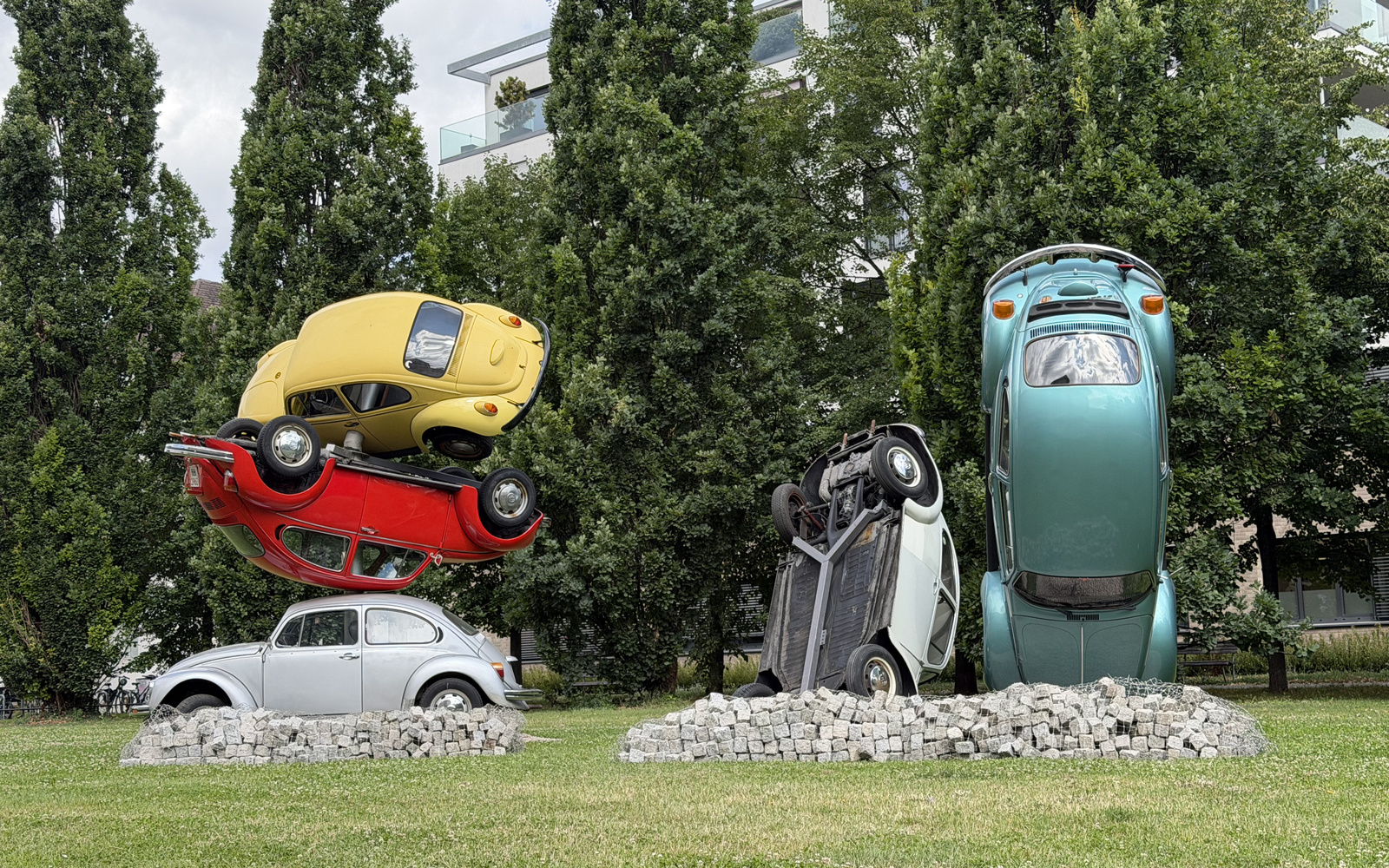 Zu sehen sind fünf unterschiedlich farbige VW-Käfer, die übereinander gestapelt sind. 