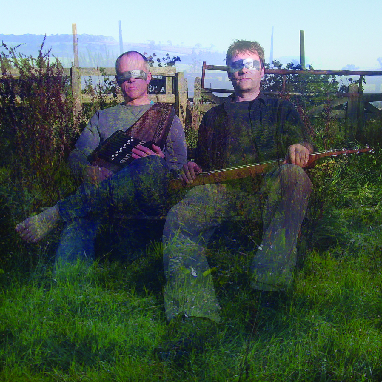 Zwei Männer sitzen mit Musikinstrumenten in der Hand auf einer Wiese, ihre Augen sind mit silbernem Klebeband verhüllt