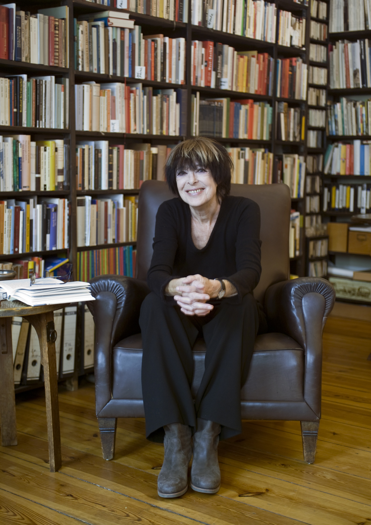 A woman is sitting in a chair in front of a large bookshelf.
