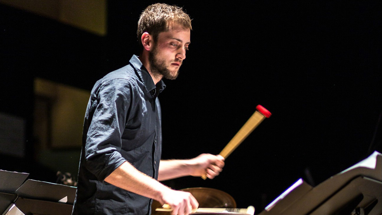 Young man with dark shirt plays on a percussion instrument.