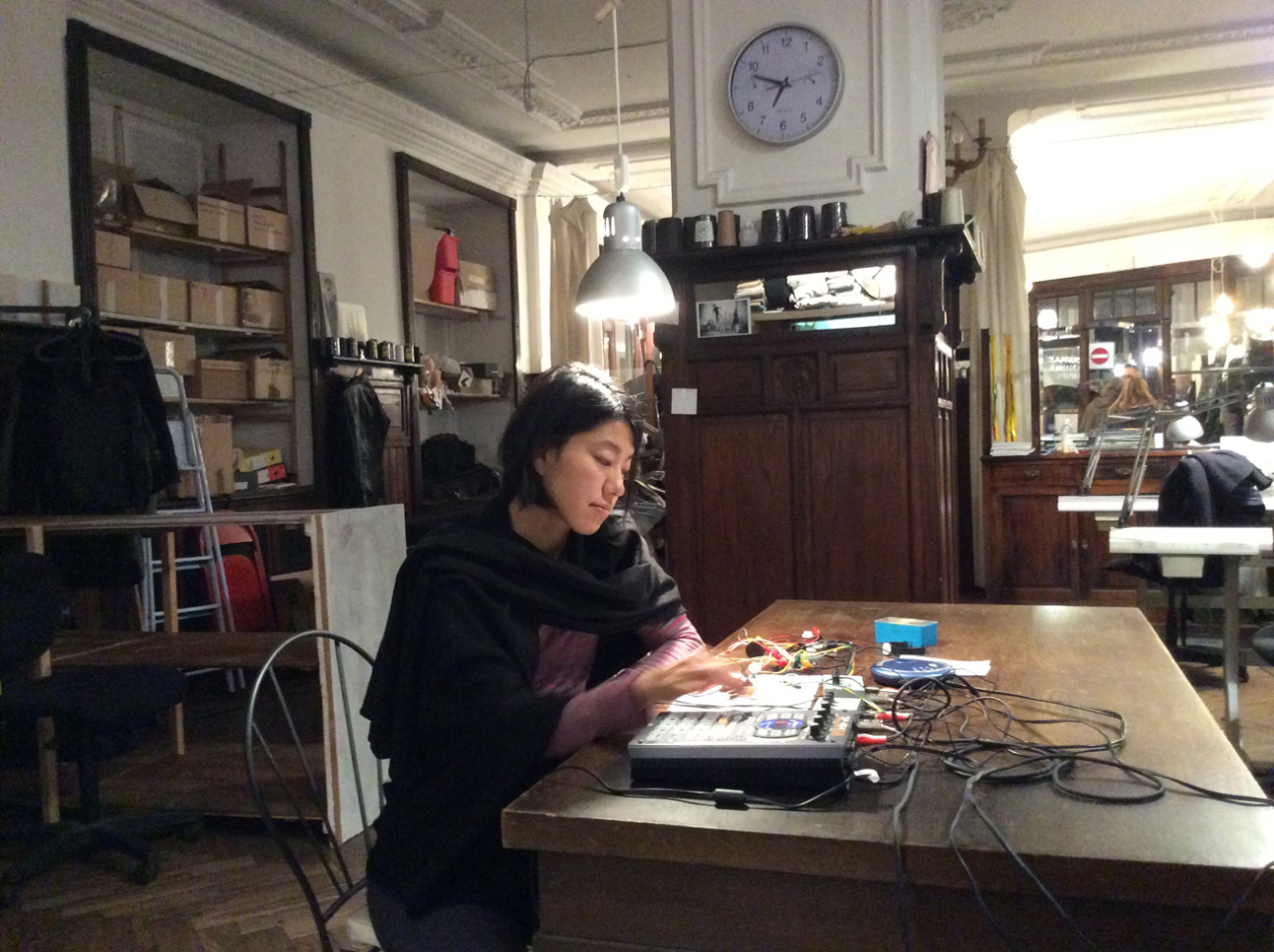 A young woman is sitting at a table in front of some technical devices. She's creating electronic music.