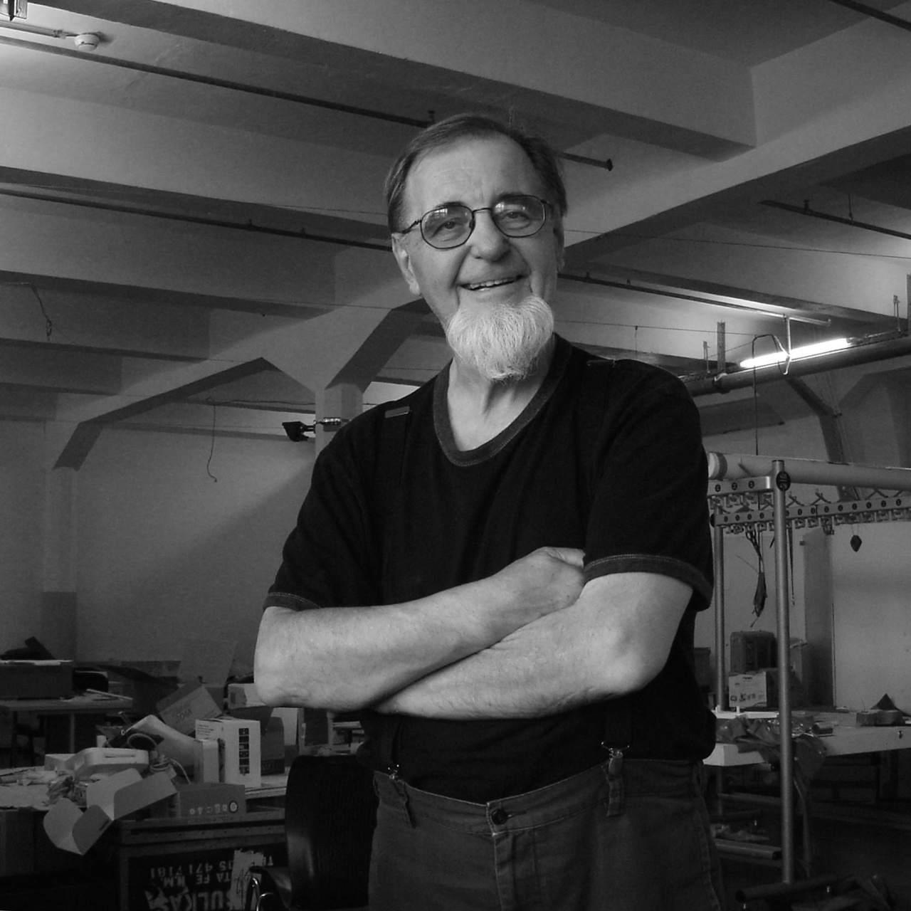 Portrait of Woody Vasulka in black and white: He stands, arms crossed, in his guest artist studio.