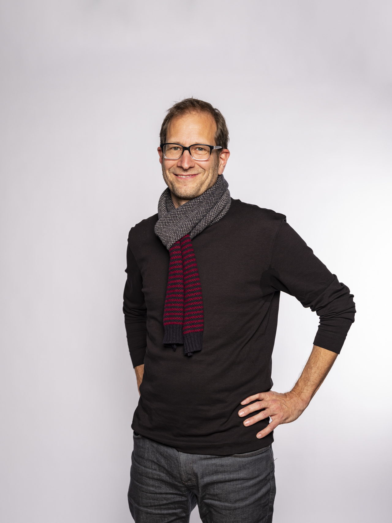standing smiling man with glasses and gray scarf