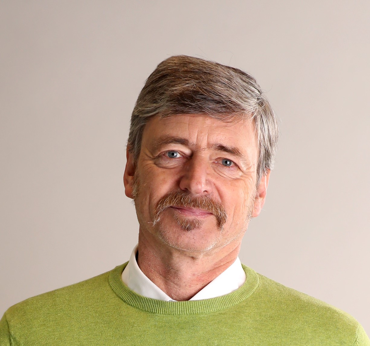 Foto eines Manns mit Schnauzbart in grünem Pullover