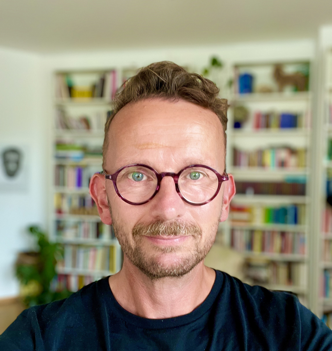 Portrait of a man with round glasses in front of a bookshelf.
