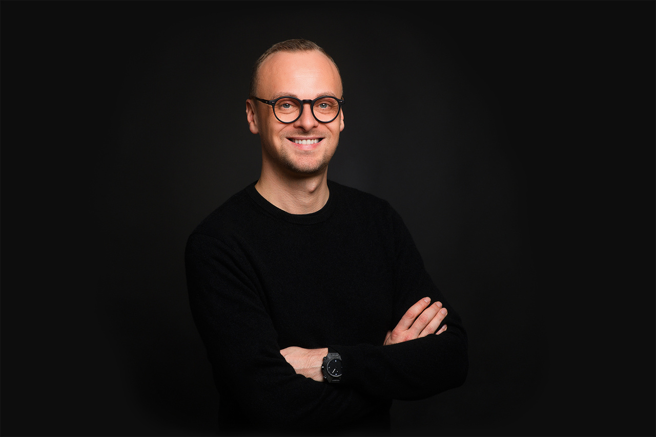 A portrait photo of a person with glasses against a black background. 