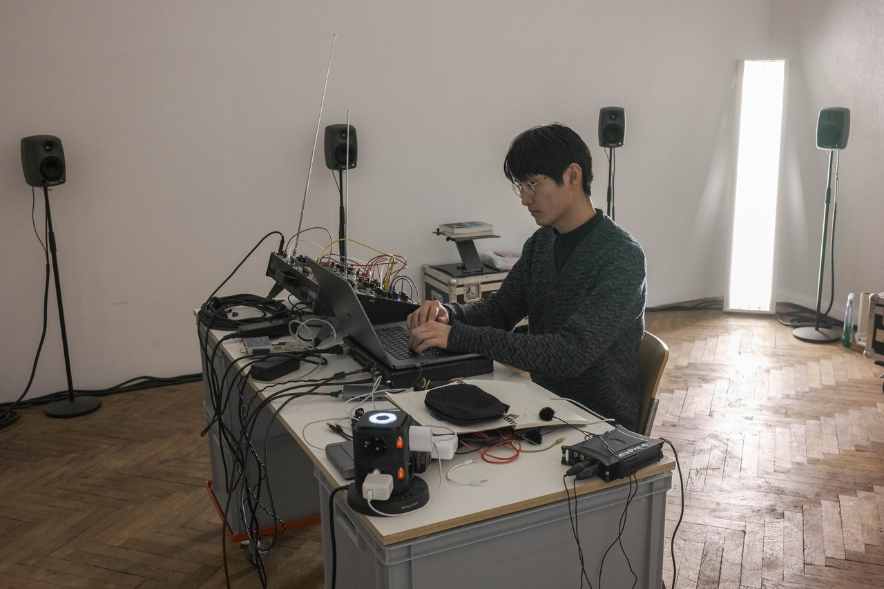 Eine sitzende Person am Laptop, umgeben von Lautsprechern.