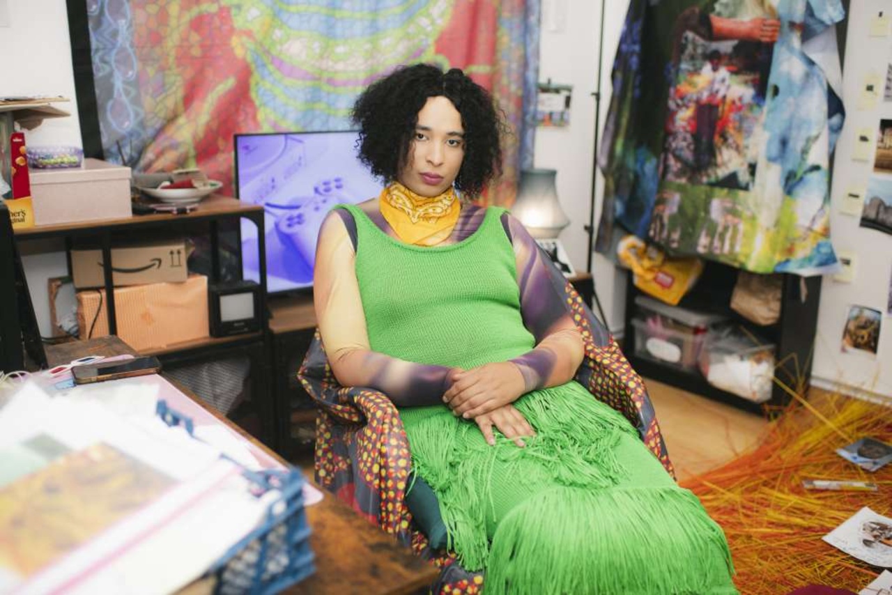 A person wears a green dress and sits in a room.