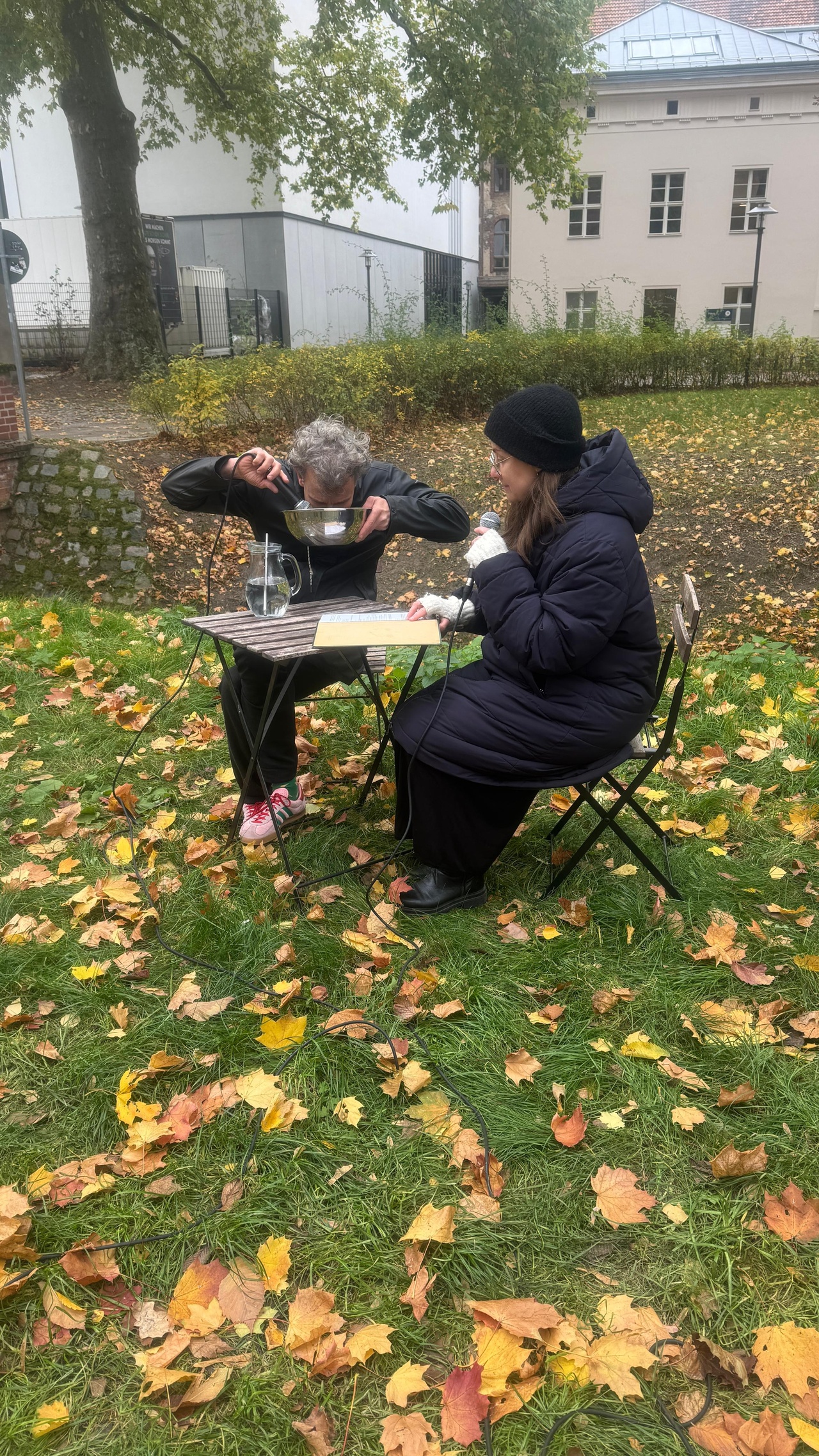 Zu sehen sind zwei Personen, die zusammen an einem Tisch im Freien sitzen. 