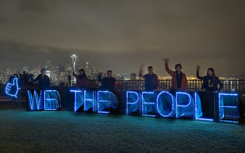 »We the people« lettering in blue light in front of a city silhouette