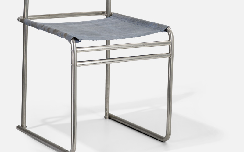 Ein Stuhl, dessen Gerüst aus Metallstangen besteht. Die Sitz- und Rückenfläche ist aus Stoff