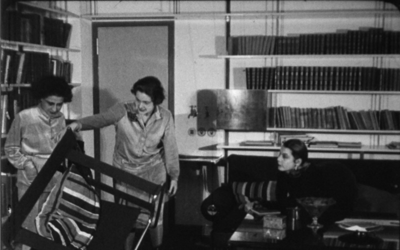 Filmstill aus »Wie wohnen wir gesund und wirtschaftlich?« von 1926 in schwarz-weiß. Darauf sind drei Frauen zu sehen, die die Möbel in einem Wohnzimmer begutachten.