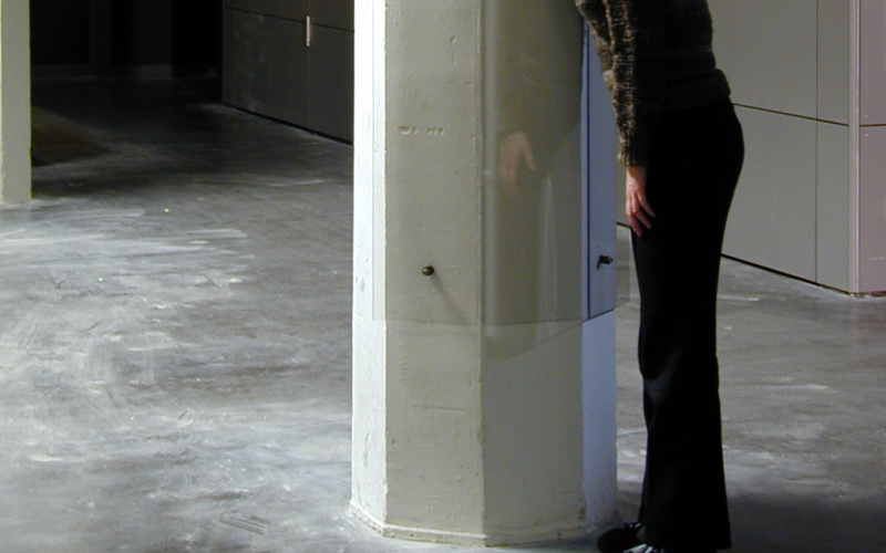 Woman presses her ear against a plexiglas loud-speaker installed on a column
