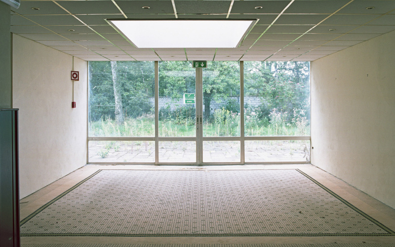 Ein leerer Raum mit großen Fensterfront mit Blick in einen begrünten Außenbereich.