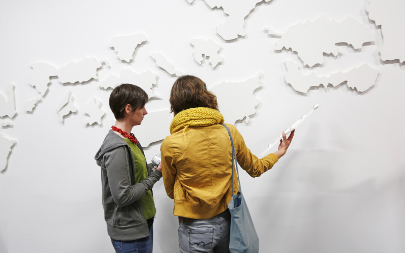 Two people in front of a white structured wall.