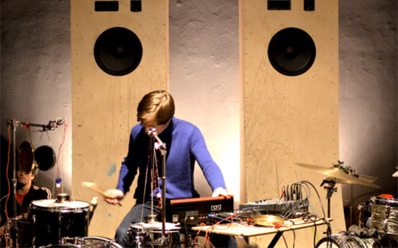 Ein Musiker in einem lila Hemd. Er bedient ein Mischpult und spielt Schlagzeug.