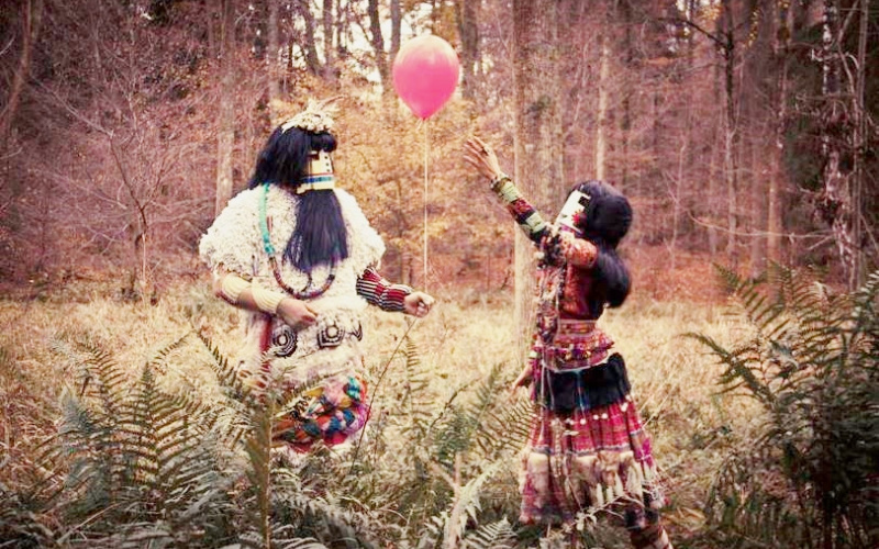 Zwei kostümierte Personen spielen auf einer Waldlichtung mit einem rosa Luftballon