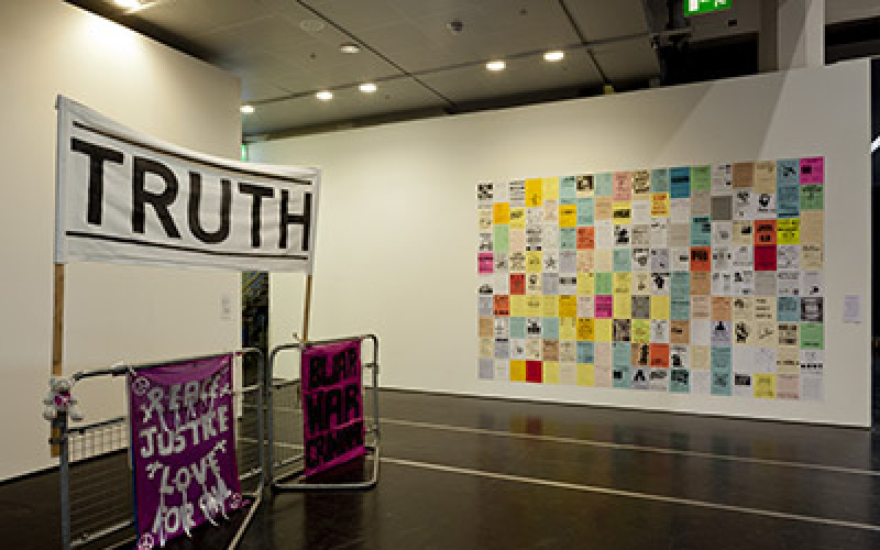 On the left half of three banners are visible. On one is 'Truth'. On the right half of the image sticking on a wall many papers. They are equipped with color and text. They form a large rectangle in their mass.