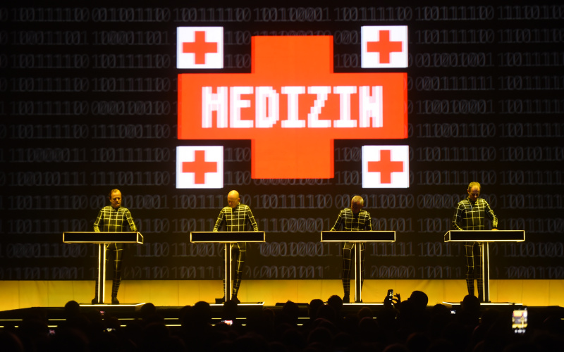 4 Männer stehen vor vier Pulten. Im Hintergrund eine Leinwand, auf der "Medizin" geschrieben steht